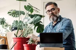 Imagem de um homem cuidando de plantas enquanto assiste aulas pelo computador.