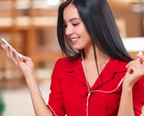 Imagem de uma moça sorrindo, com fones de ouvido e um celular na mão.