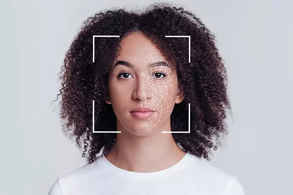Imagem colorida de uma mulher negra vestindo uma camiseta branca. O fundo é cinza e claro. Sob o rosto, uma marcação de escaneamento que identifica a localização da face.