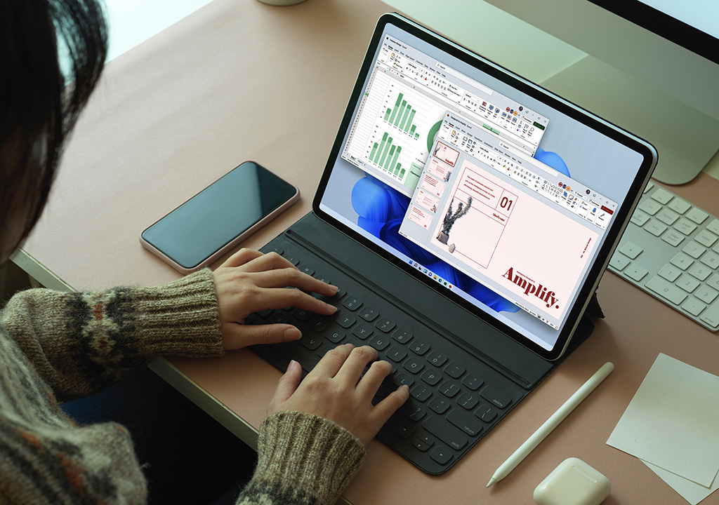 Pessoa usando Power Point e Excel em um Microsoft Surface com alguns gadgets em cima da mesa