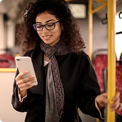 Mulher jovem sorrindo, em pé no ônibus, usando o celular.