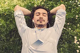 Imagem de um rapaz deitado na grama com fones de ouvido.