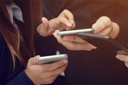 Imagem das mãos de três pessoas diferentes segurando celulares.