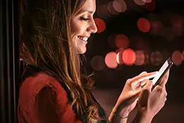Imagem mulher jovem sorrindo e olhando para o celular.