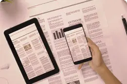 Jornal físico e, sobre ele, um tablet e um celular mostrando na tela a imagem do mesmo jornal.