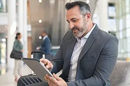 Imagem de um rapaz fazendo consultas num tablet num ambiente de aeroporto.
