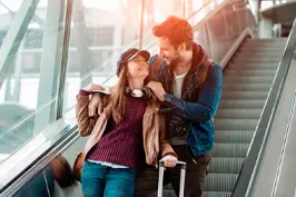 Um casal descendo por uma escada rolantes de um aeroporto.