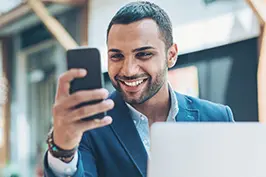 Imagem de um homem usando terno sorrindo olhando para um smartphone.
