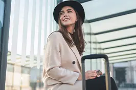Imagem de uma moça sorrindo, casacos, chapéu preto e uma mala.
