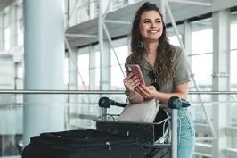 Mulher sorridente em aeroporto com um smartphone em mãos.