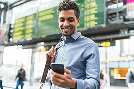 Imagem de um rapaz fazendo consultas num smartphone num ambiente de aeroporto.