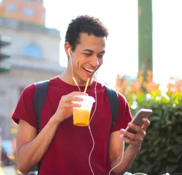 Rapaz sorrindo, ouvindo música com fones de ouvidos brancos e mexendo no celular. 