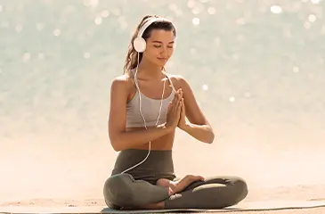 Uma moça jovem meditando de olhos fechados e fones ouvidos.