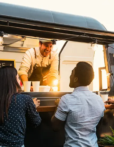 Imagem de um homem atendendo dois clientes em um food truck.