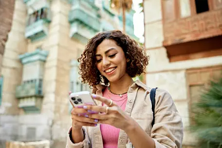 Imagem de uma moça de cabelos curtos sorrindo usando o smartphone.
