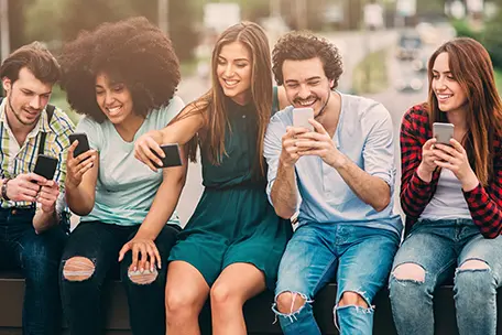 Grupo de jovens sorrindo com celular nas mãos.