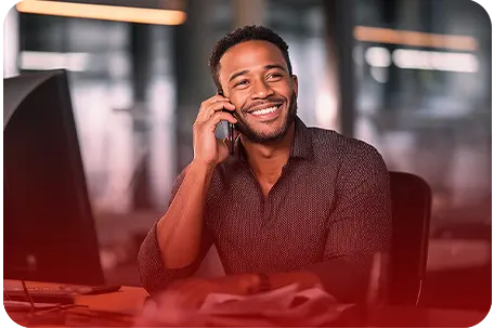 Homem sorridente olhando para uma tela de notebook com algumas folhas de papel na mão.