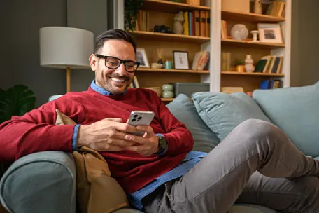 Imagem de um homem sentado no sofá com o celular nas mãos.