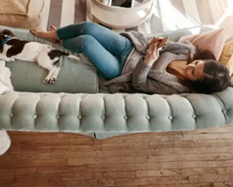 Uma moça e um cachorro deitados no sofá verde enquanto mexe no celular.