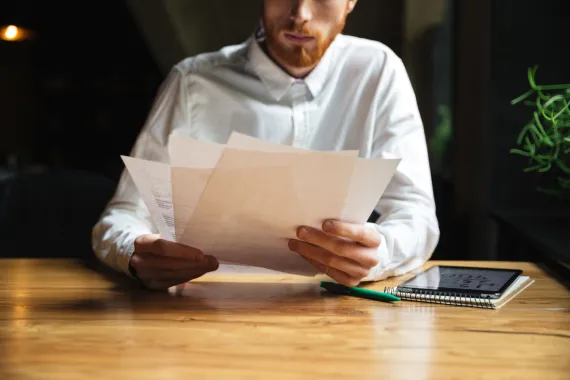 Imagem de homem sentado à mesa com papéis nas mãos.