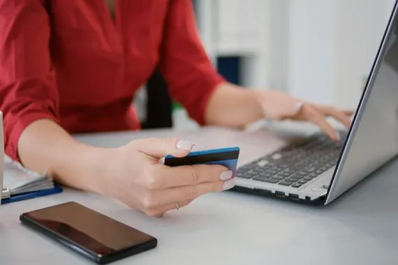 Imagem de uma mulher com cartão de crédito nas mãos e notebook.