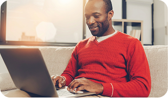 Homem de blusa vermelha usando um notebook no sofá